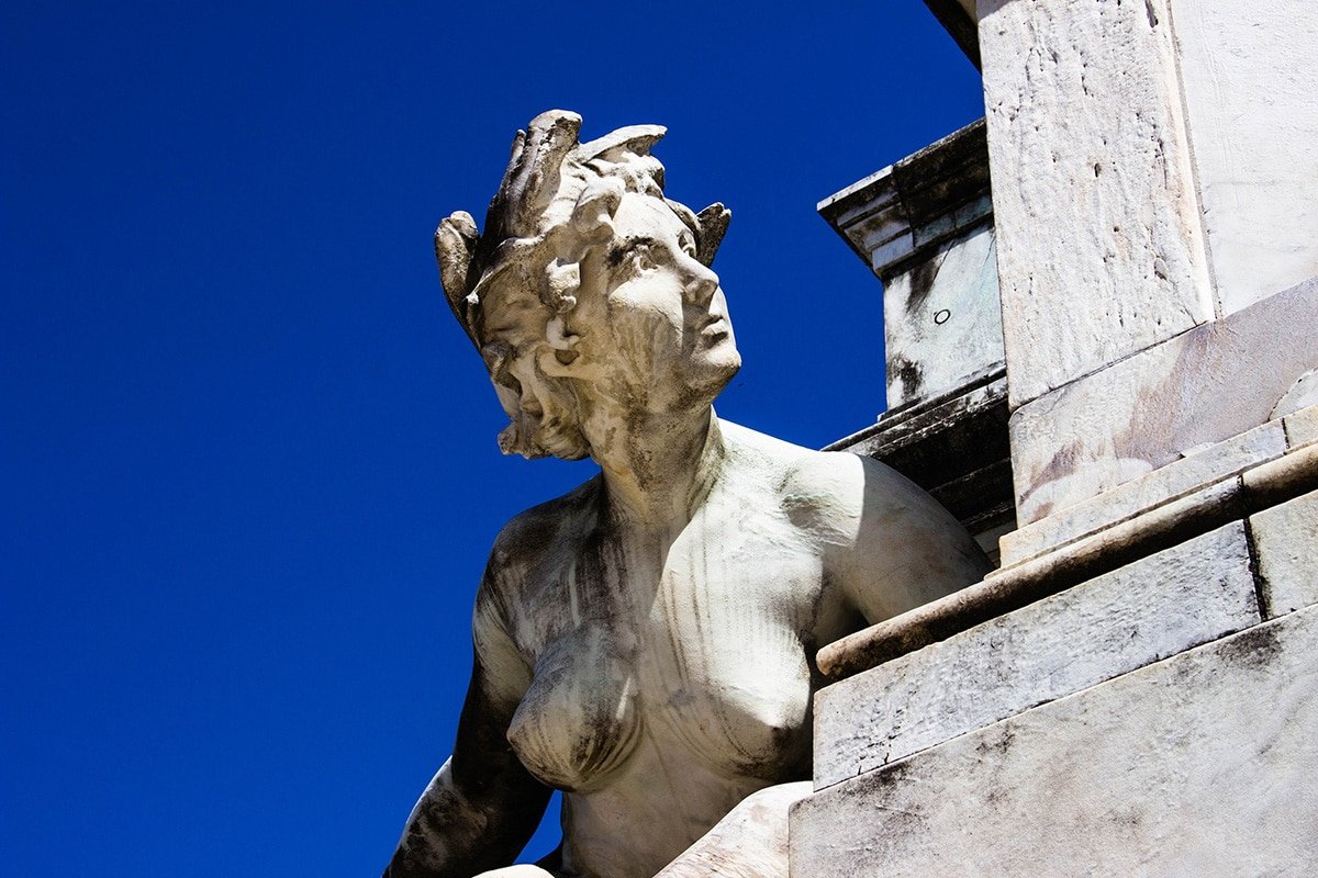 A photograph of a white female Renaissance statue against a stark blue sky.